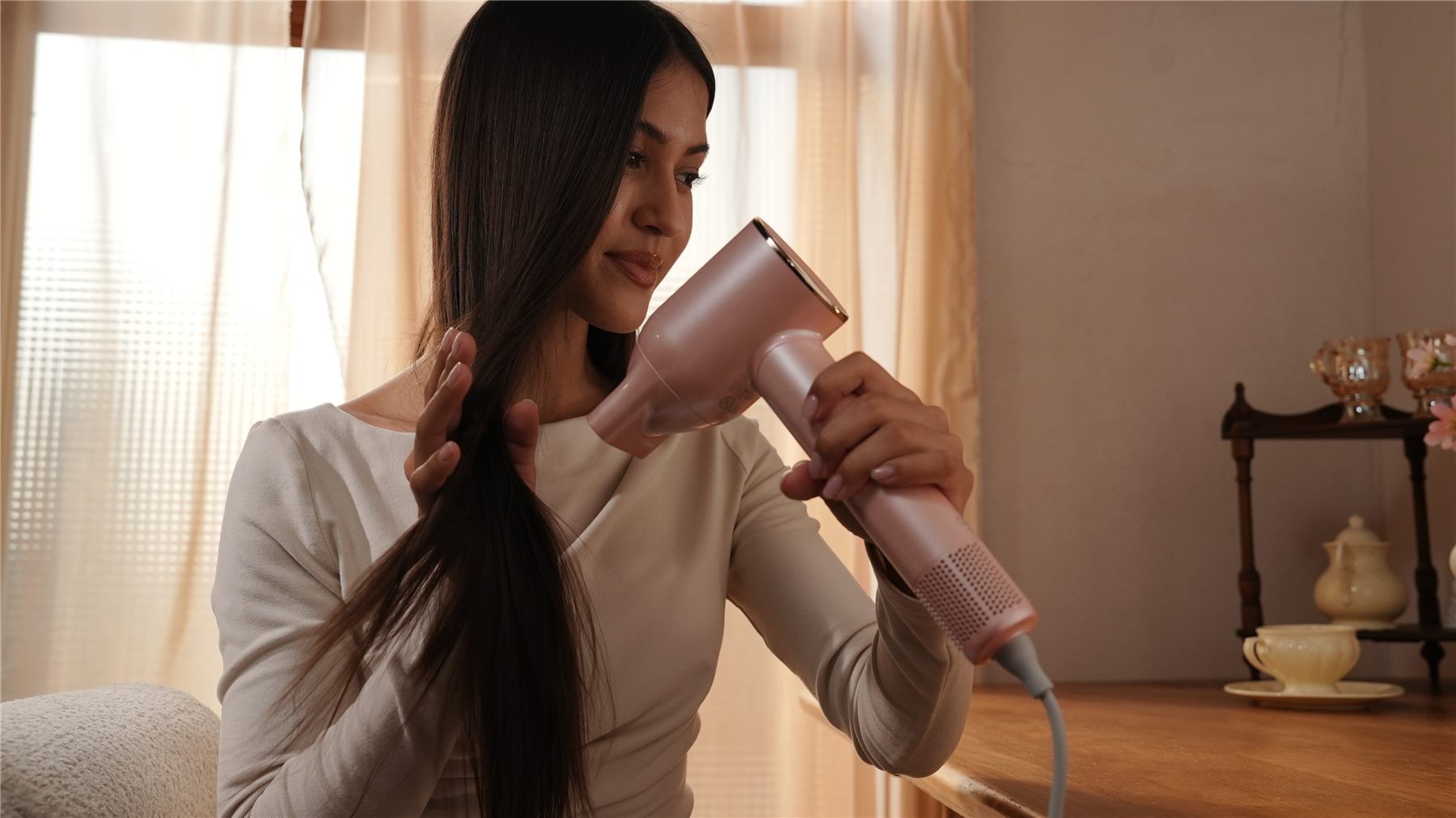 Woman with long dark hair smoothing it while using the OHM Ultra+ plasma hair dryer